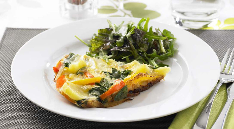 A slice of vegetarian frittata on a plate with a side salad